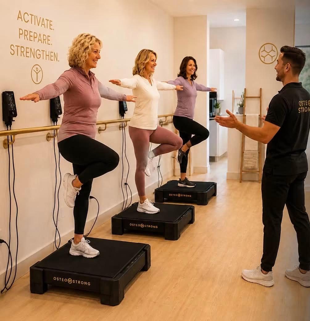 Three members balancing on one leg on OsteoStrong VibePlates while a coach guides them